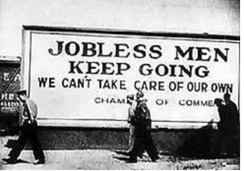 Black and white image of men walking with their heads down while a billboard behind them reads, "jobless men keep going - we can't take care of our own"