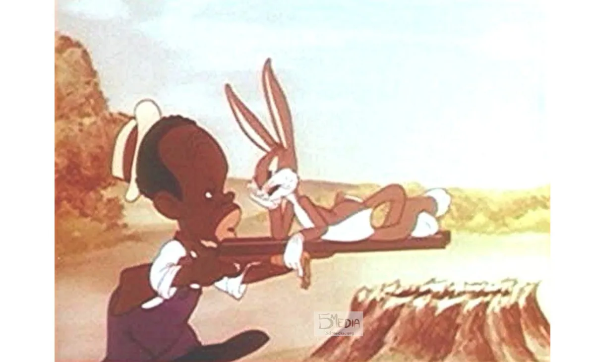 A still shot from a 1940’s short called All This and Rabbit Stew featuring Bugs Bunny laying on a shotgun that is held by a Black character who is illustrated with exaggerated and racist characteristics