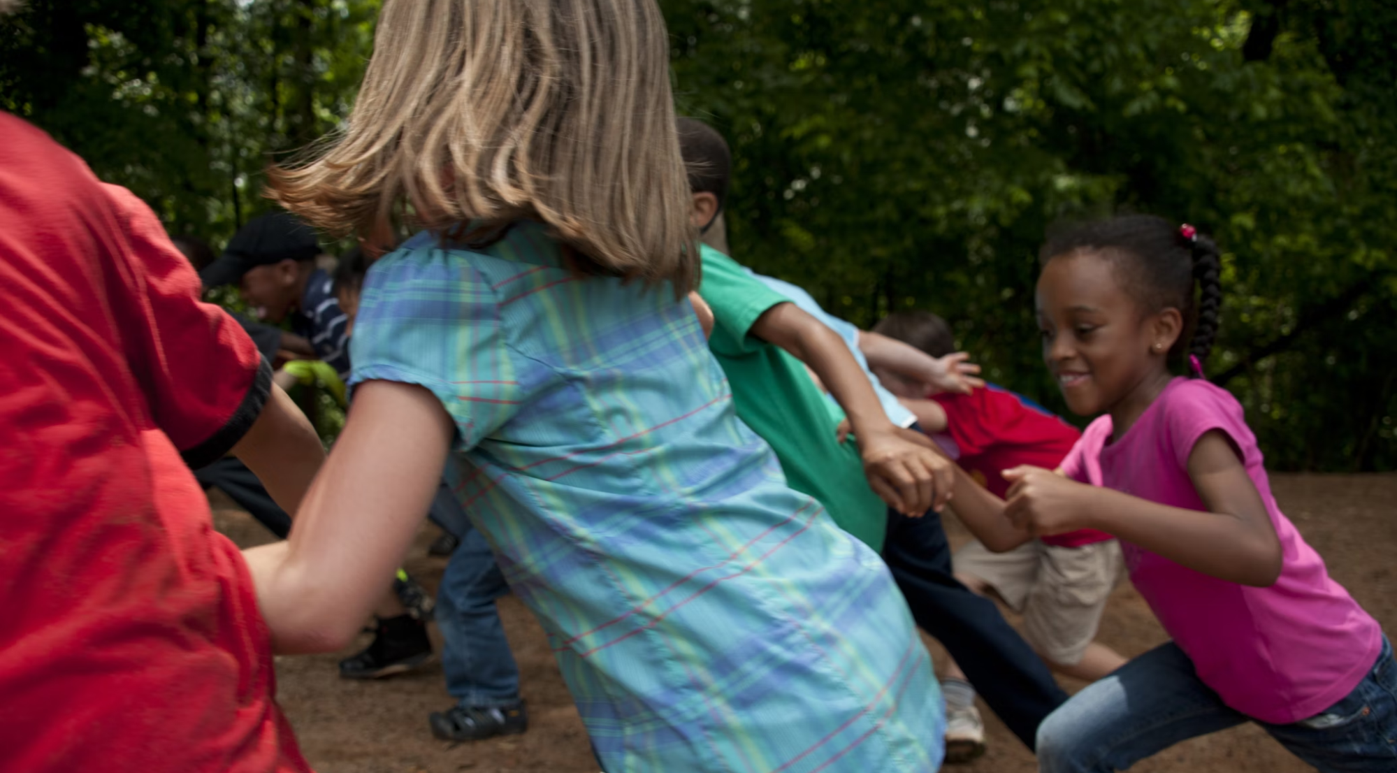 Several children of different races and ethnicities are running through the woods playing together