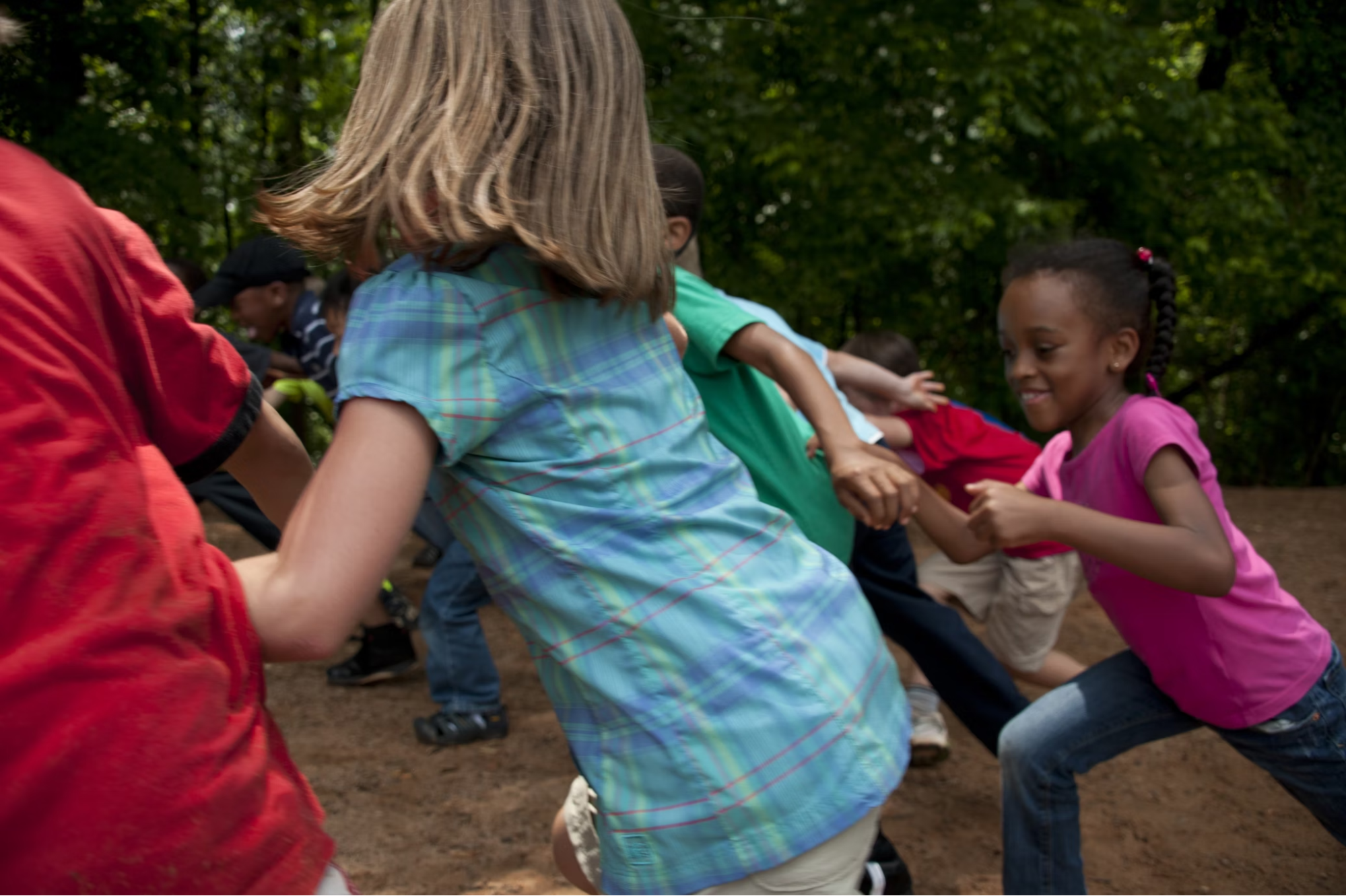 Several children of different races and ethnicities are running through the woods playing together