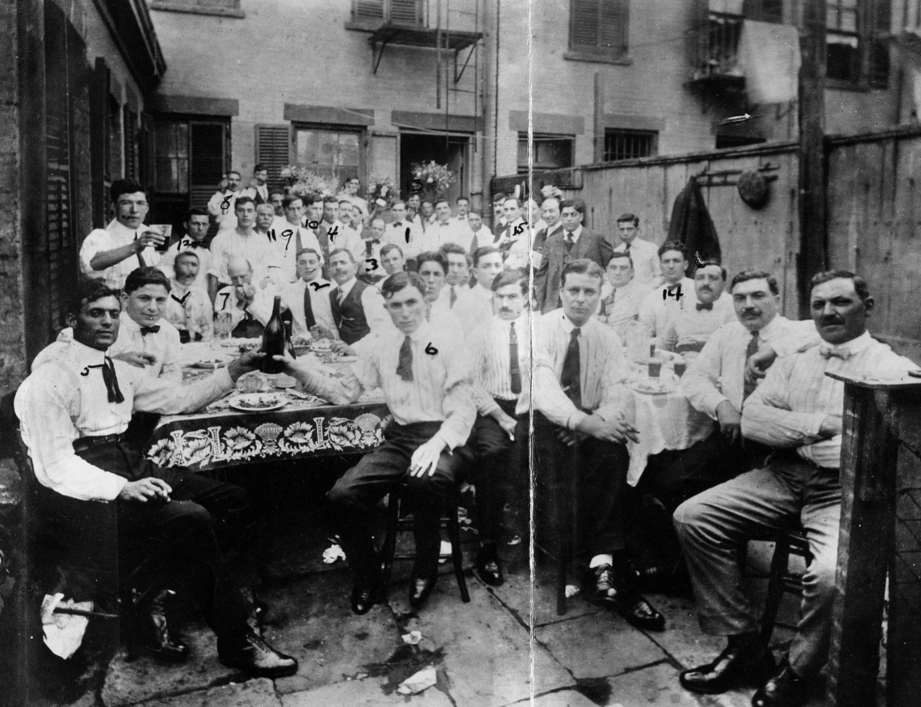 Black and white image of young men wearing matching pants and white shirts with ties as they socialize together