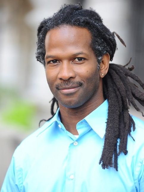 Professional photo of neuroscientist Carl Hart wearing a blue button up and his dreadlocks pulled back behind his head