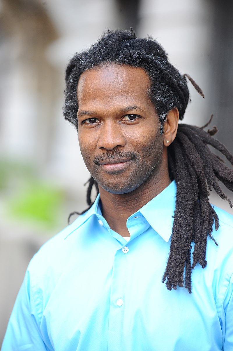 Professional photo of neuroscientist Carl Hart wearing a blue button up and his dreadlocks pulled back behind his head