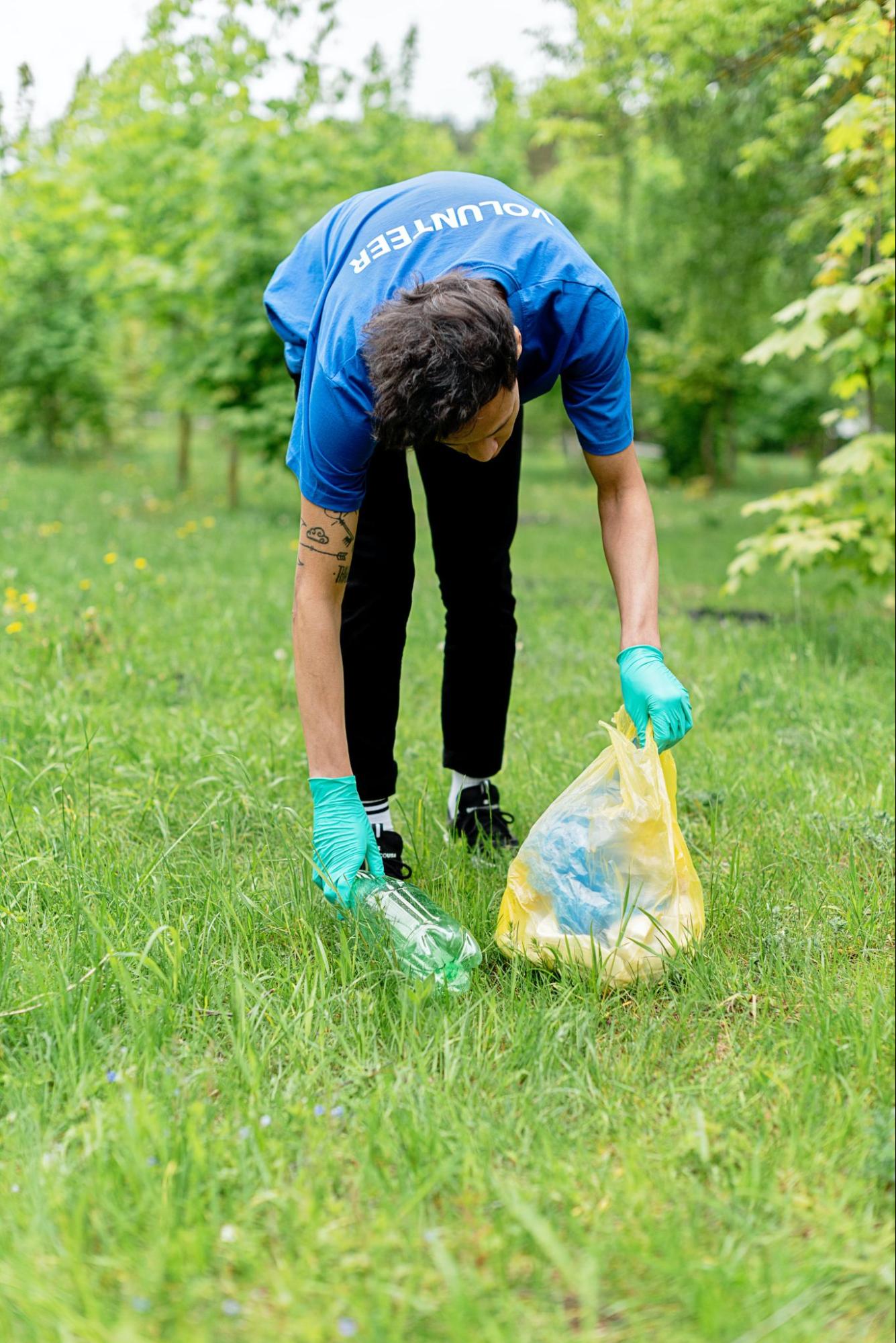 A person wearing gloves and a shirt that says "volunteer" picks up some trash in a field