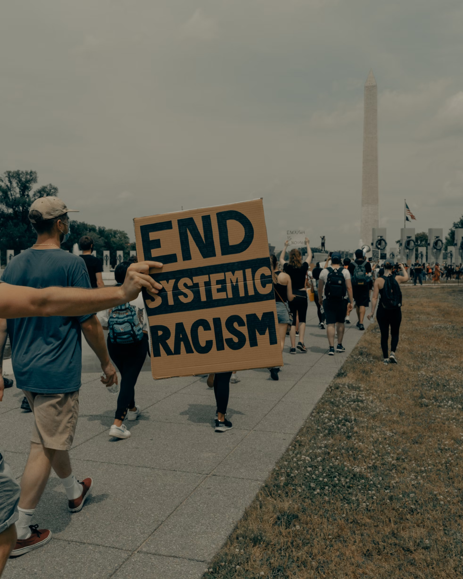 Protestors marching in front of the Washington Monument with one holding a sign that says, "end systemic racism."