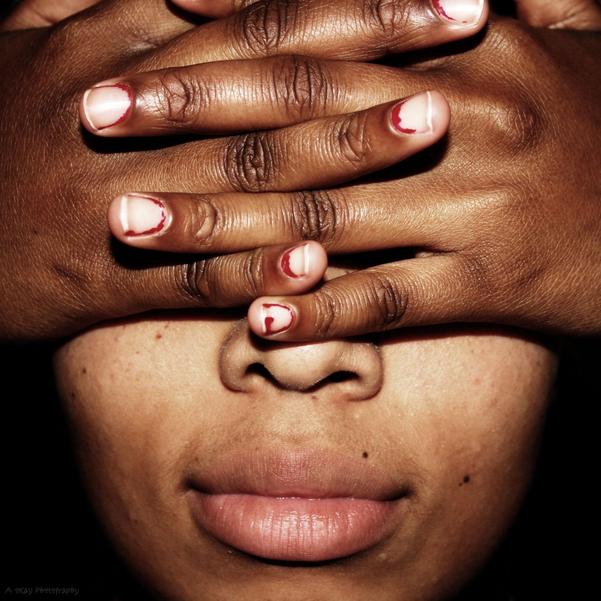A person with dark skin tone covers their eyes with their hands, with a blank facial expression