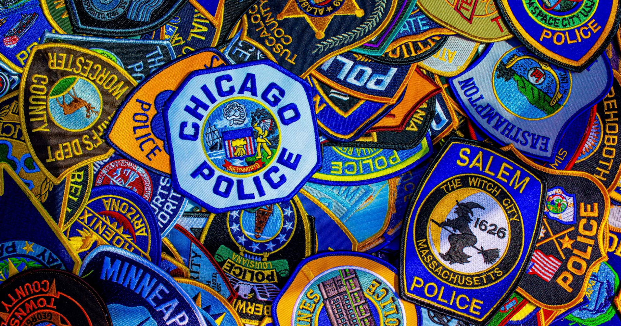 Vibrant and colorful photo of a variety of police agency patches - such as Chicago Police, Salem Police, and Minneapolis Police - strewn about on a table