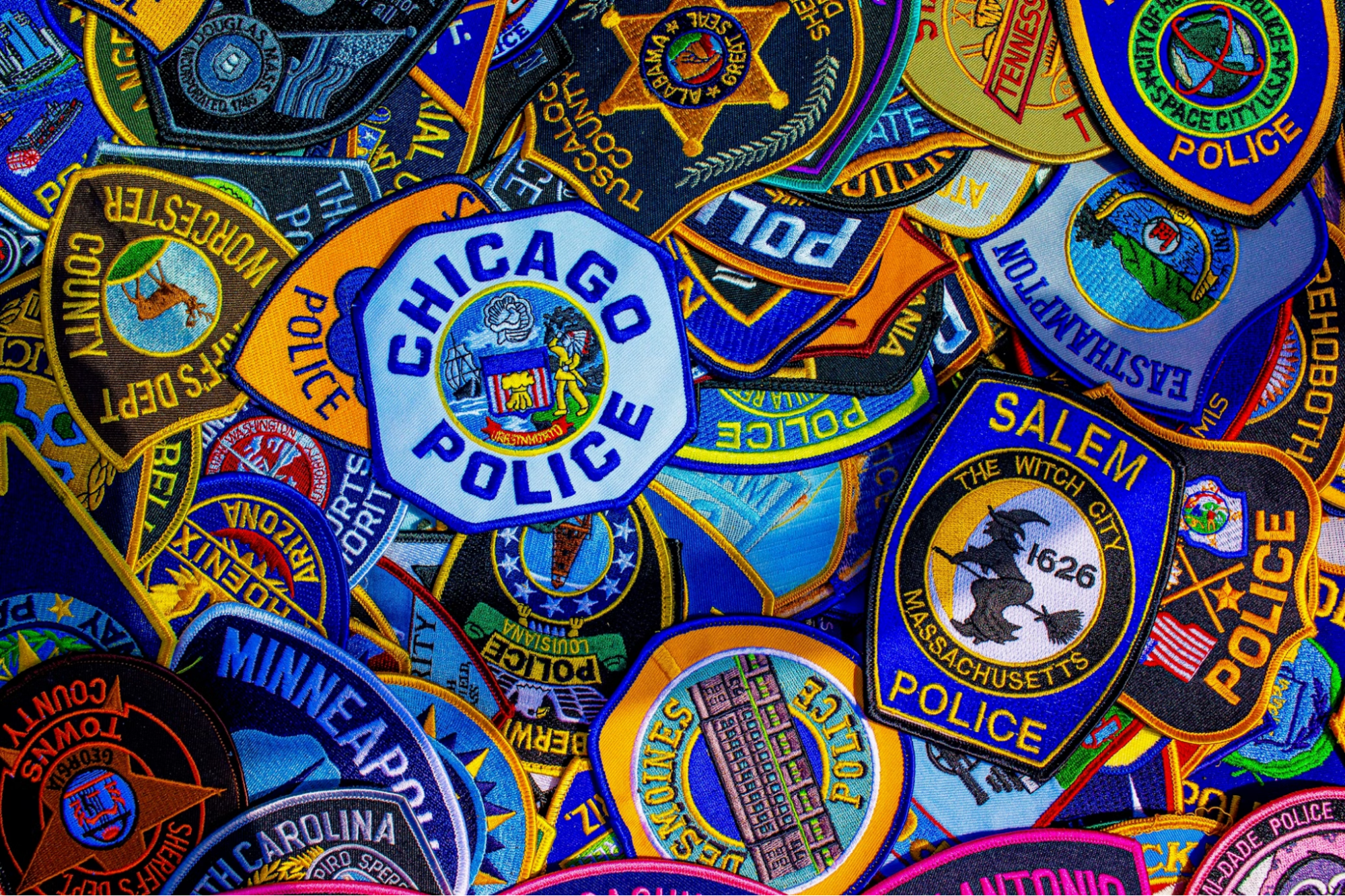 Vibrant and colorful photo of a variety of police agency patches - such as Chicago Police, Salem Police, and Minneapolis Police - strewn about on a table