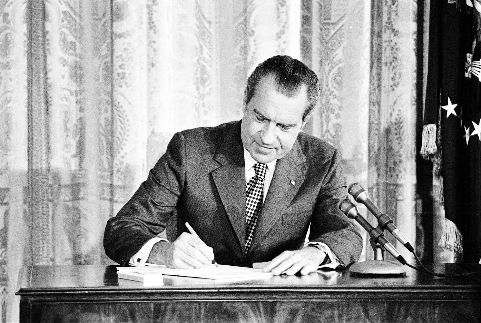 Black and white image of Richard Nixon in a suit at his desk signing The Drug Abuse Office and Treatment Act of 1972