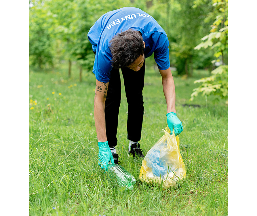 A person wearing gloves and a shirt that says "volunteer" picks up some trash in a field