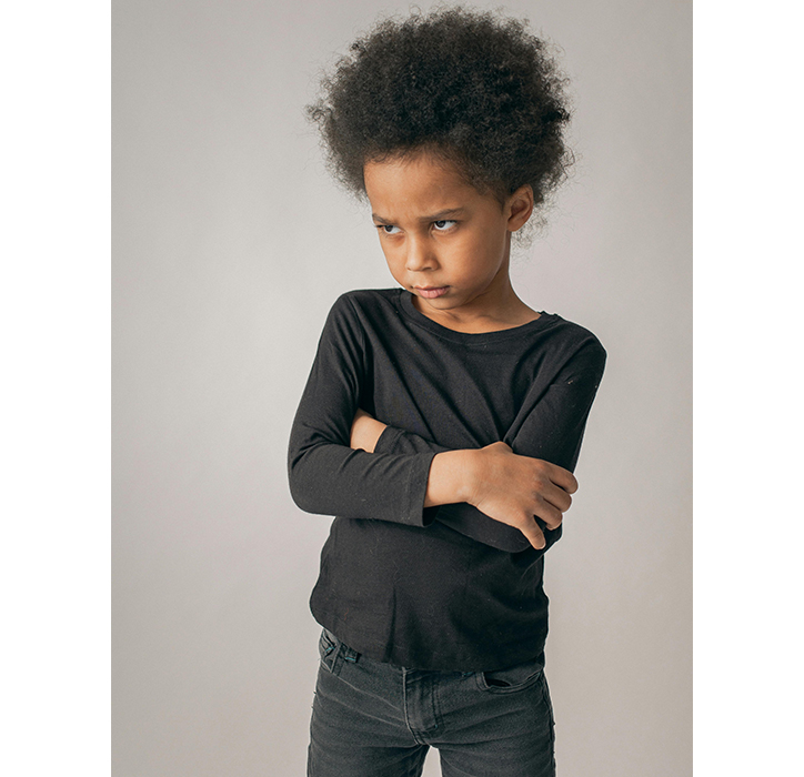 A Black child stands with their arms crossed and an upset look on their face