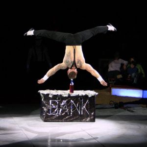 A person balances up-side down on their head on the top of a glass wine bottle.