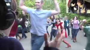 Amy smiling and raising her hands as she watches people dancing in the street