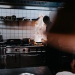 In a kitchen, flames are rising from a pan next to a person.