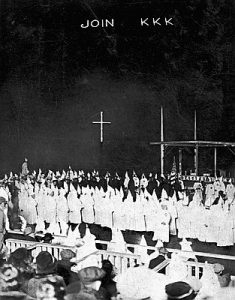 Photo of a large KKK meeting, with people wearing white robes and hoods with crosses in the background. Text at the top reads, "Join KKK"