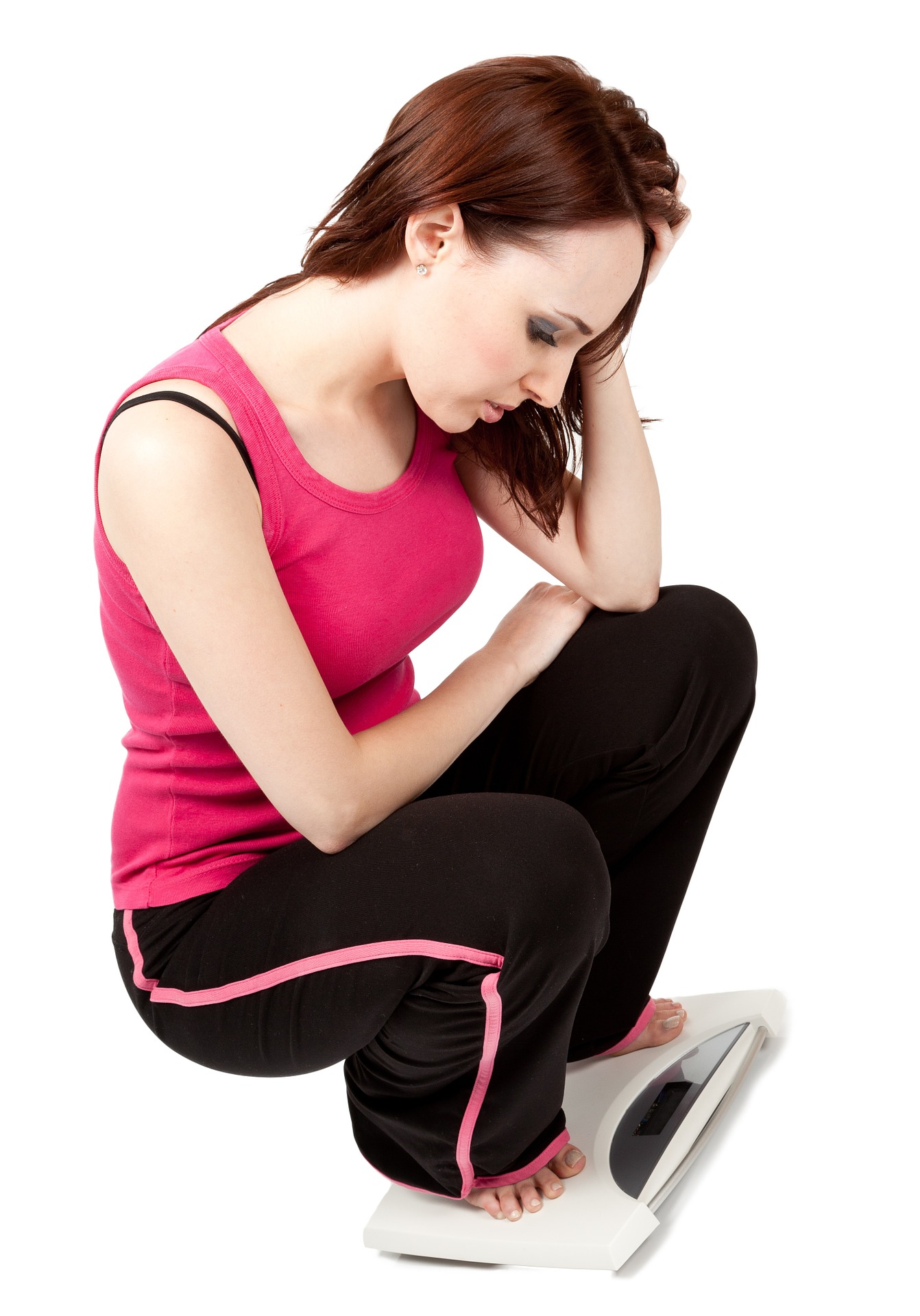 A young woman with a worried look on her face is squatting down while standing on a bathroom scale.