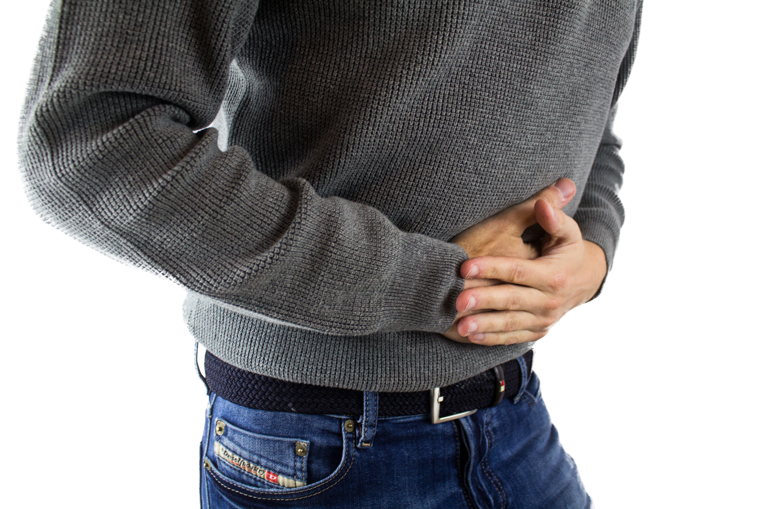 A photograph of a person's torso, appears to be a man, his hands clasped over his abdomen as if in pain.