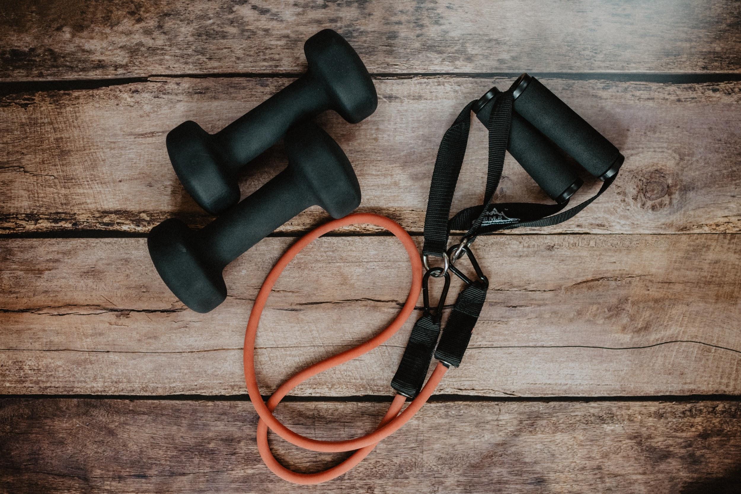 A set of small free weights and a resistance band are shown on a wooden table top.